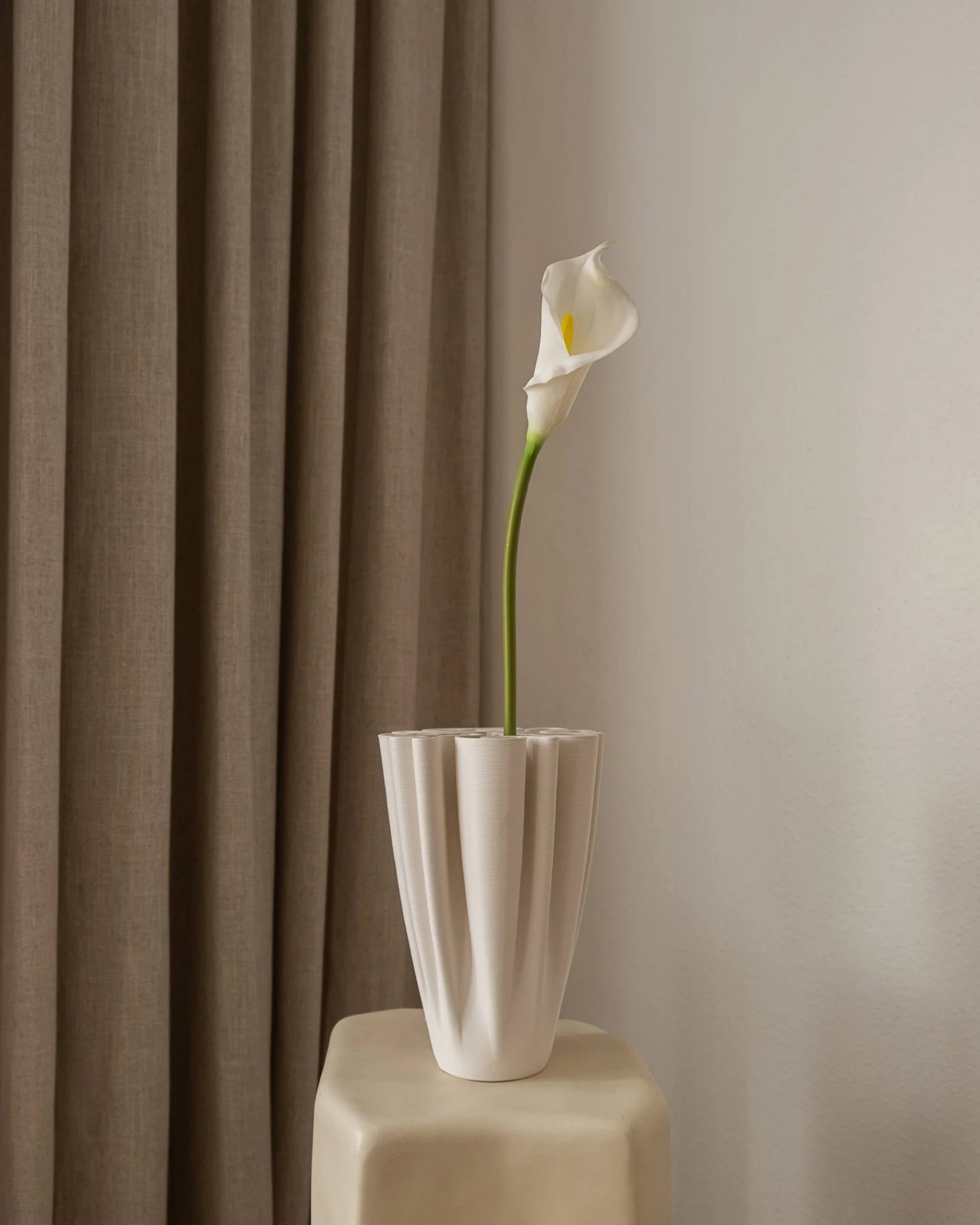 Amarante Calla Lilje i hvit, kunstig blomst med grÞnn stilk og gul midte i hvit plissert vase pÄ kremfarget pidestall