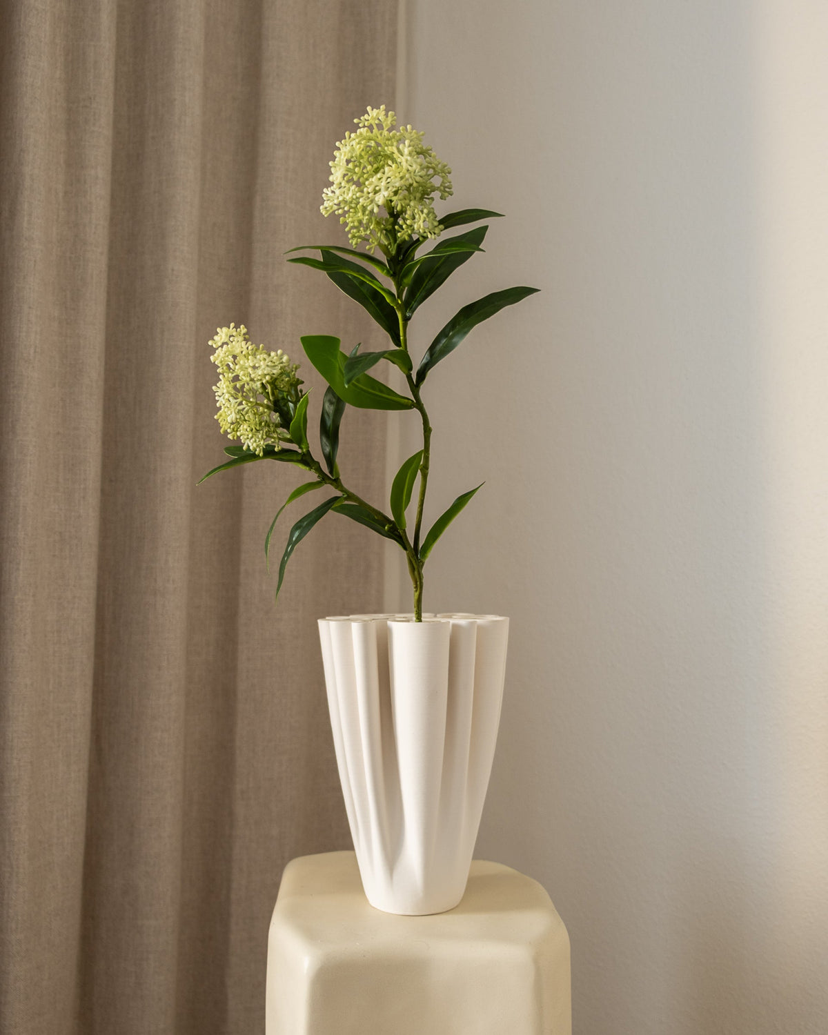 Amarante Skimmia Bærgren Hvitgrønn kunstig blomst med grønne blader og lys hvitgrønne blomster, i hvit vase på pall