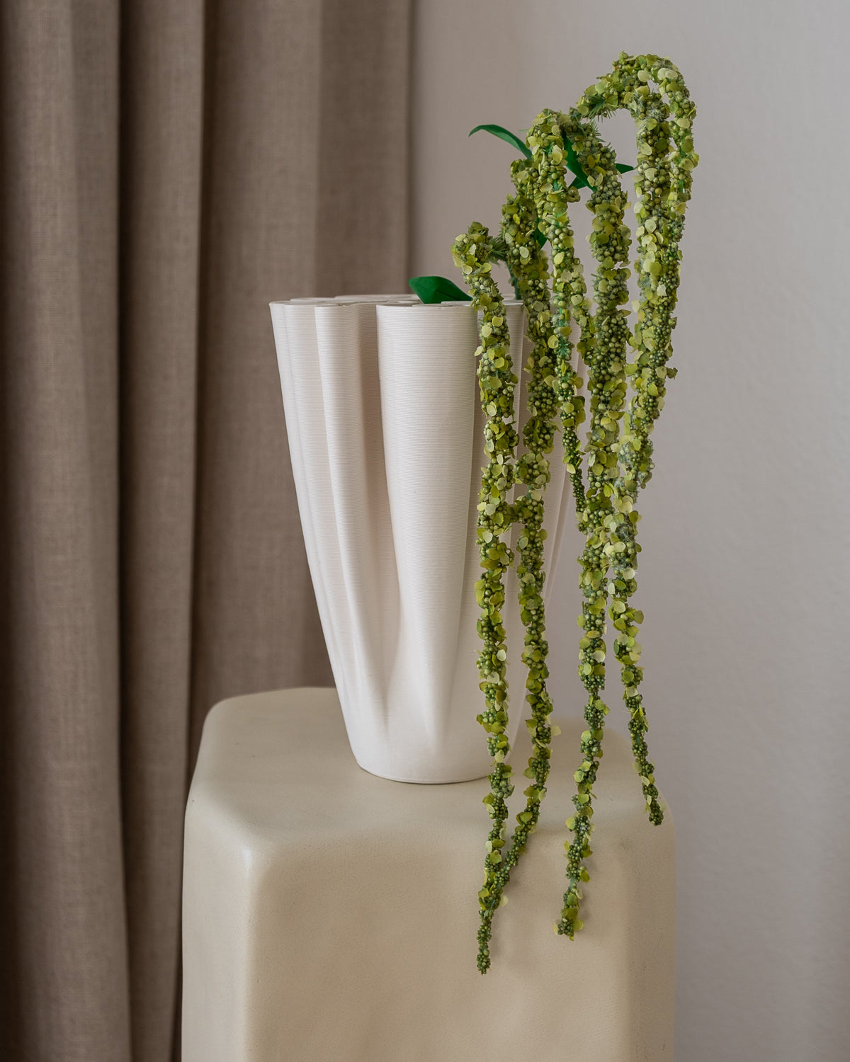 Amarante Amaranthus kunstig blomst, grønne drue-lignende stilker i hvit riflet vase, på beige pidestall