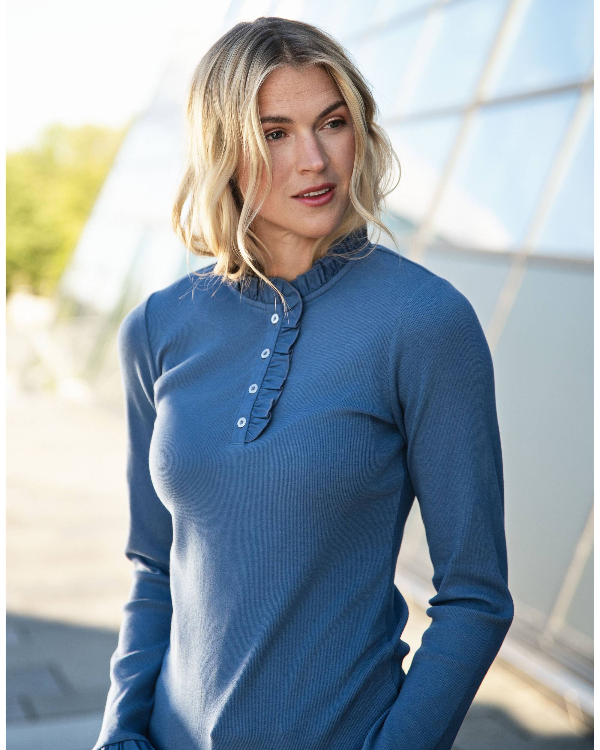 Modell iført mørkeblå Close to My Heart Flory T-shirt, viser hals og bryst med rysjer og hvite knapper. Ute.