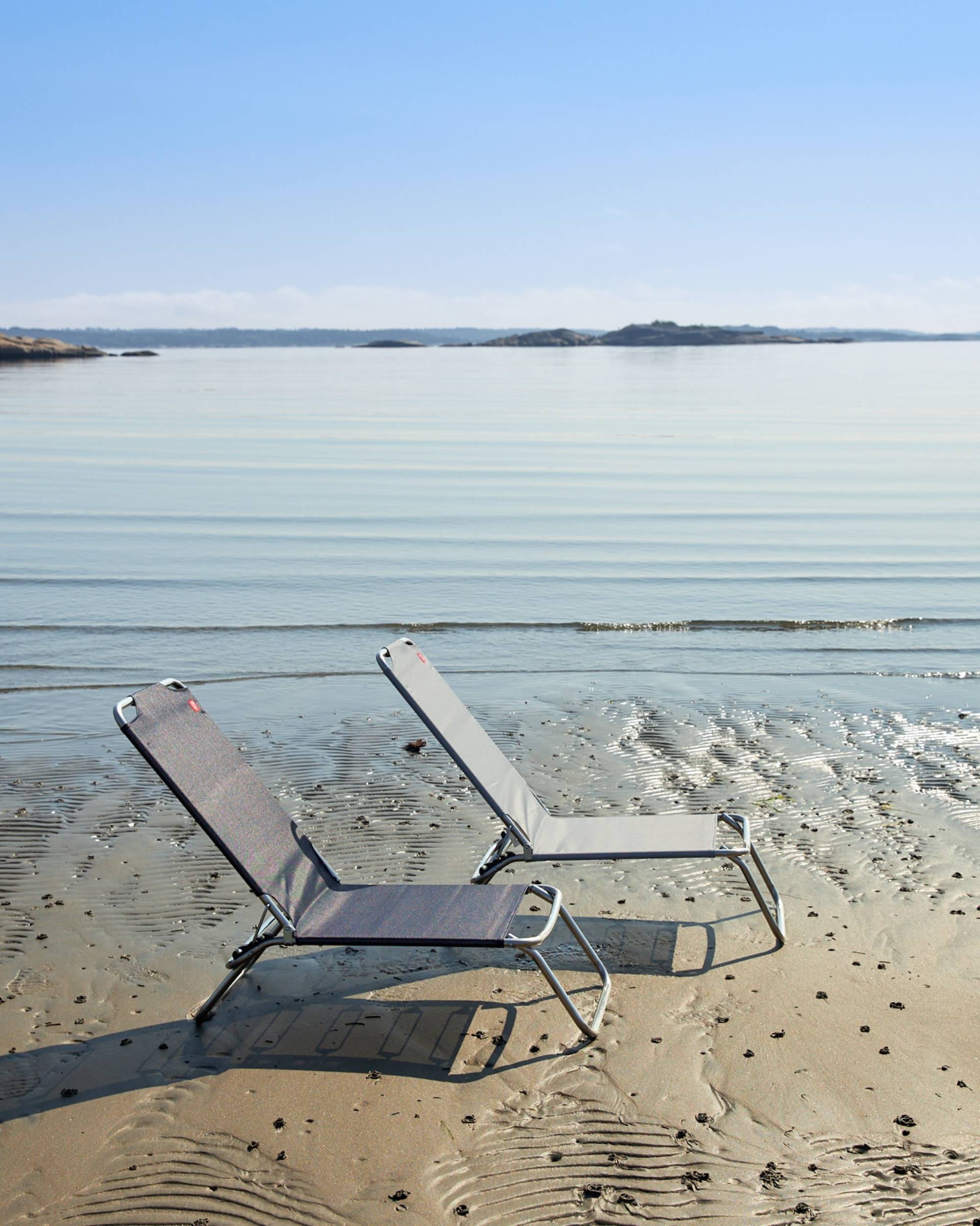 Fiam Jolly strandstol, sett bakfra, mørk og lys grå texfil-tekstil, aluminiumsramme på en strand ved vannet
