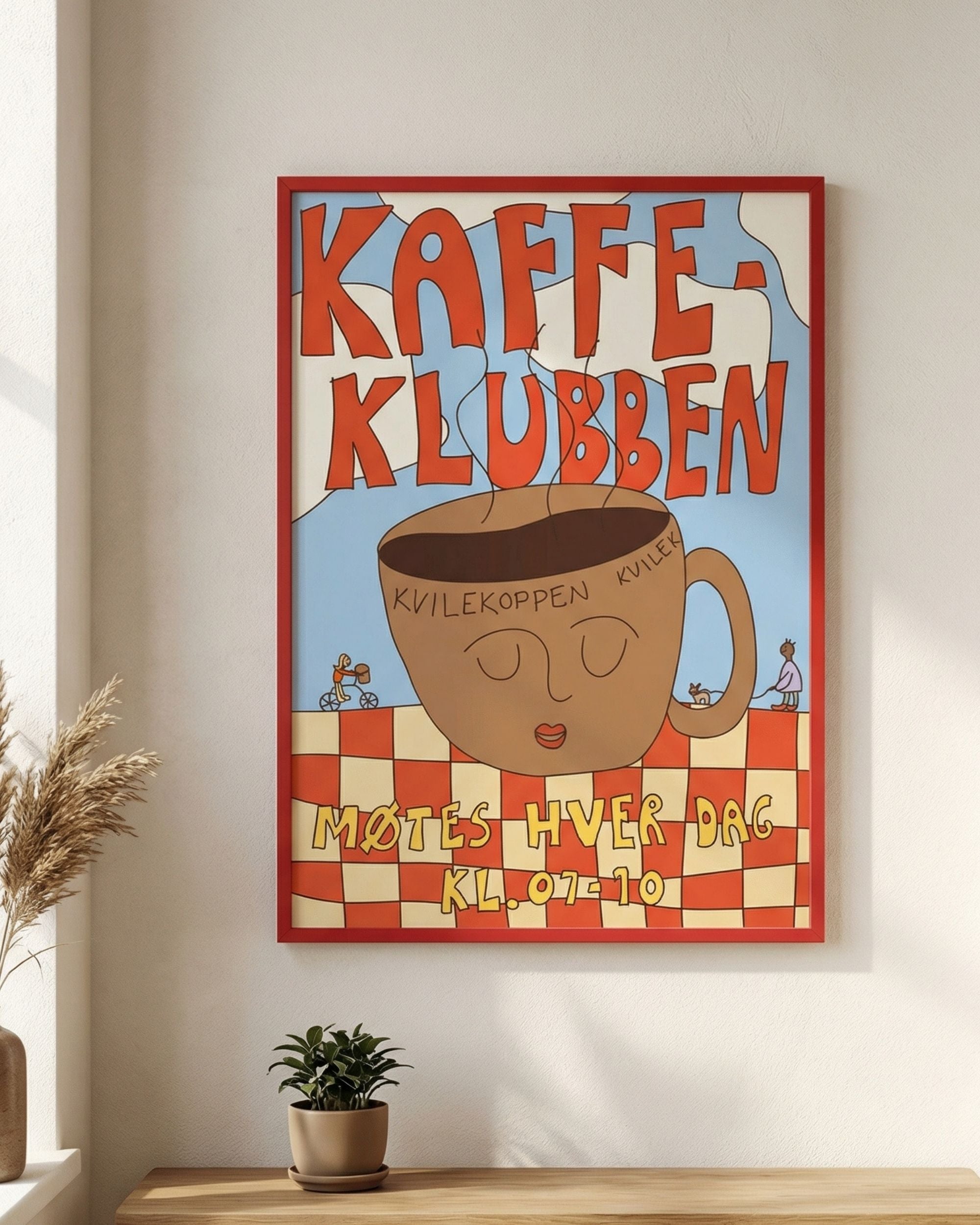Printbydale Kaffeklubben print i rød ramme på vegg, med lekent design av stor kaffekopp på rød/gul-rutet bakgrunn.