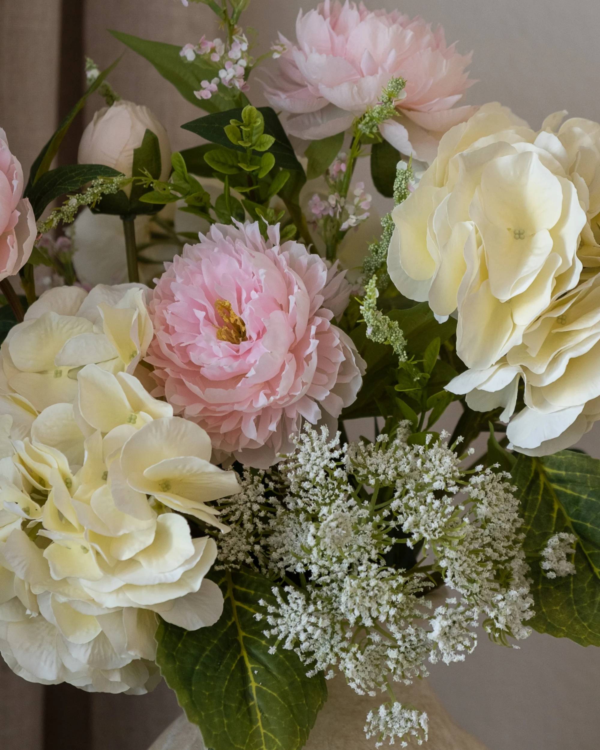 Nærbilde av Amarante Strawberry Creme bukett med detaljerte rosa pioner, kremfargede hortensia og grønne blader.
