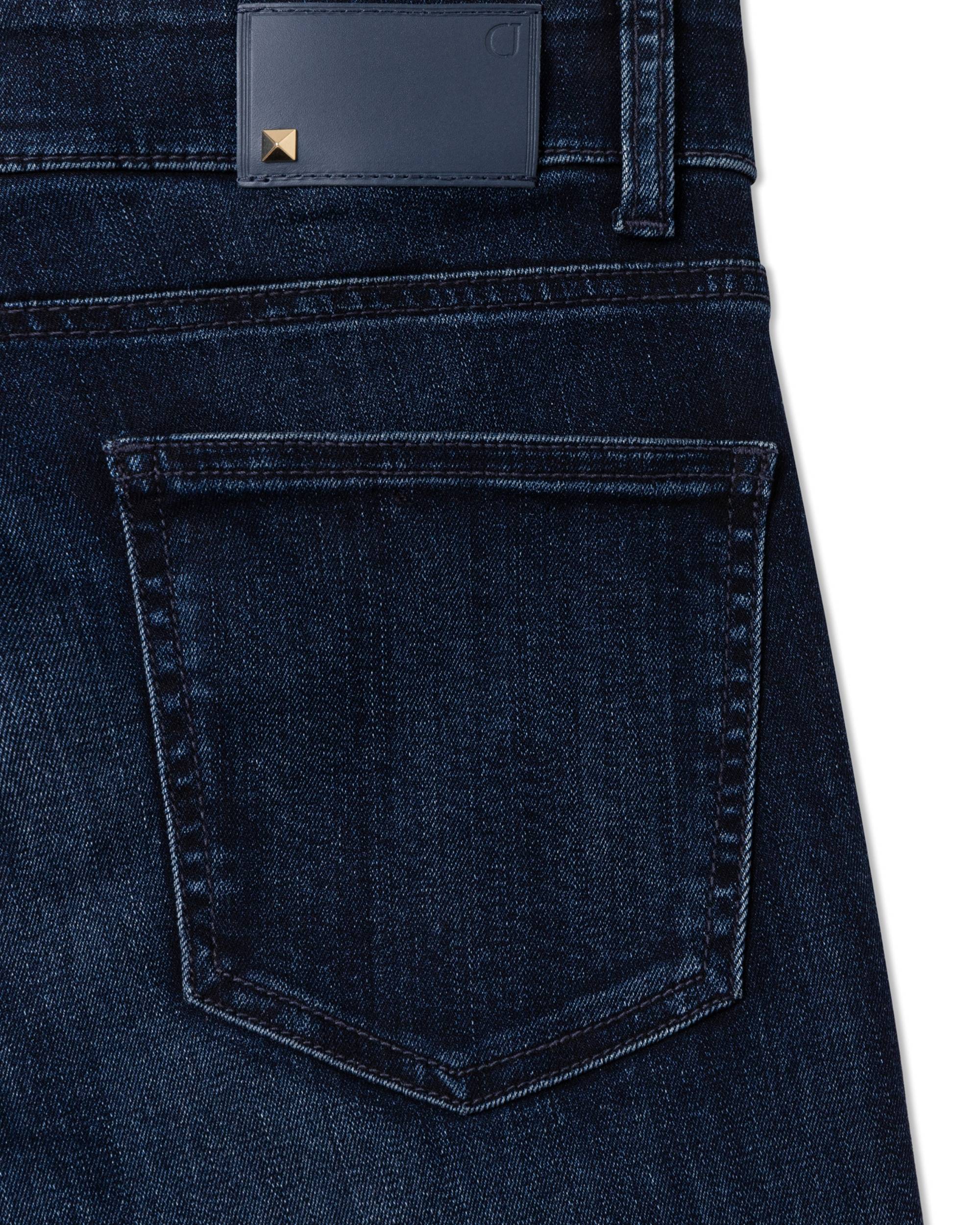 Cambio Tessa bukse, detalj av mørk blå denimmateriale med baklomme og brunt merke med gullnagledetalj